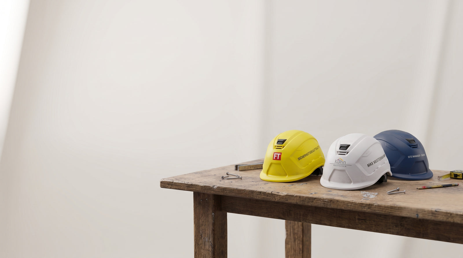 Drei personalisierte Bauhelme mit Firmenlogo und Namen – gelb, weiß und blau